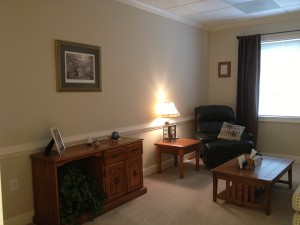 therapy room in west cobb location. leather chair in right corner. wooden table and dresser in center. tan carpeted floor.